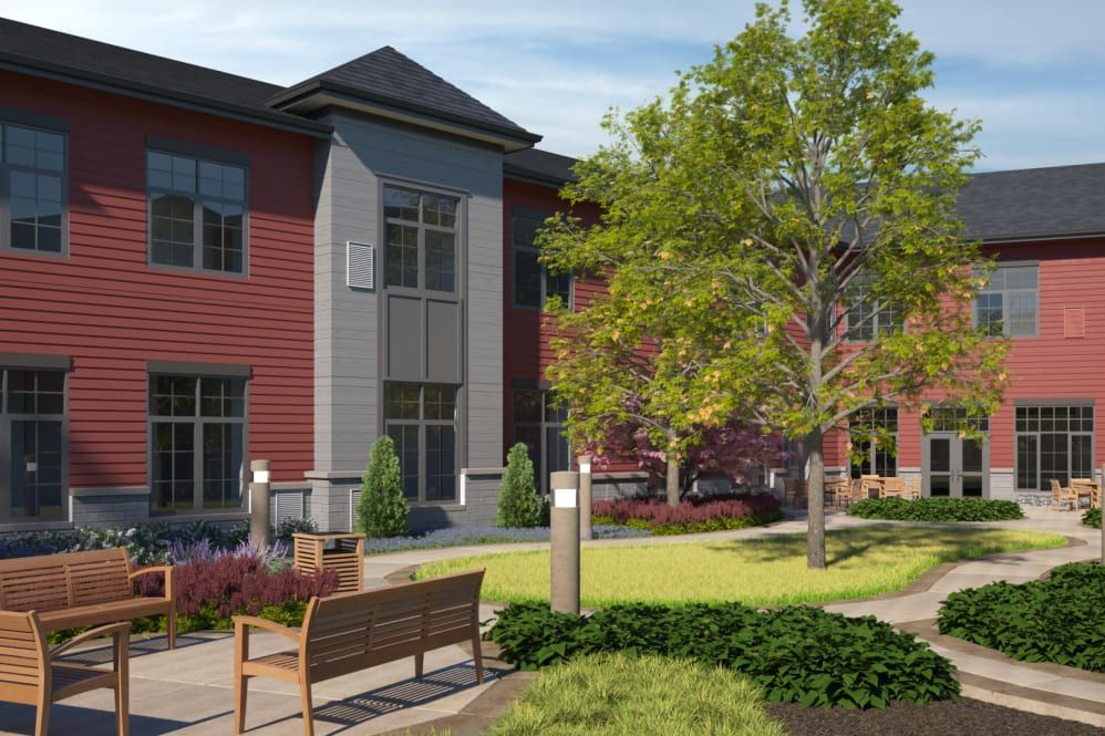 A modern residential building with red and gray exterior, surrounded by landscaped greenery and benches.