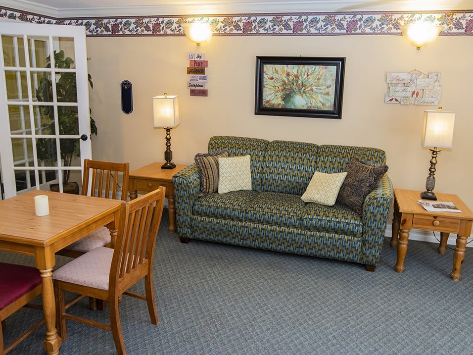 A cozy living room with a patterned sofa, wooden dining table and chairs, and decorative wall art.