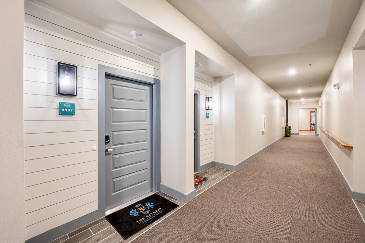 A well-lit apartment hallway with gray doors and a doormat.