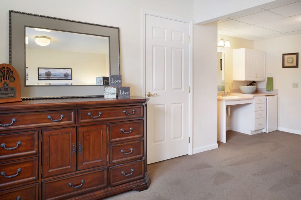 A cozy bedroom featuring a wooden dresser with a mirror, leading to an adjoining bathroom.