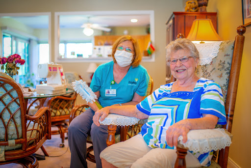 A caregiver smiles alongside an elderly woman in a cozy living room setting.
