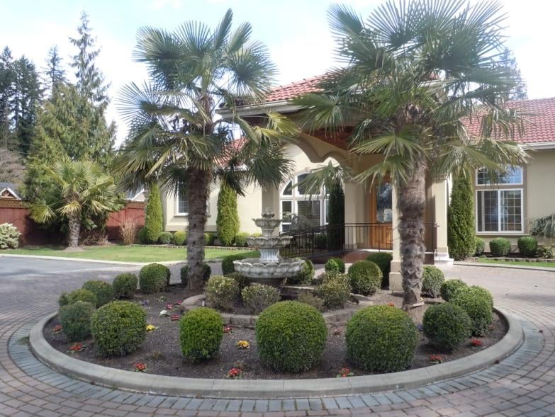 A beautifully landscaped area with a central fountain, surrounded by palm trees and neatly trimmed bushes in front of a large building.