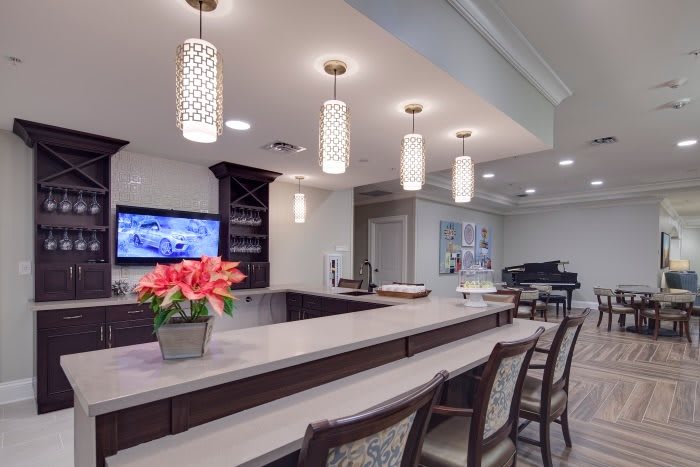 A modern bar interior with stylish pendant lighting, a seating area, and a flower arrangement, featuring a piano and television in the background.