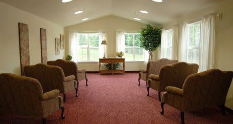 A bright waiting room with chairs arranged around a carpeted area and large windows letting in natural light.