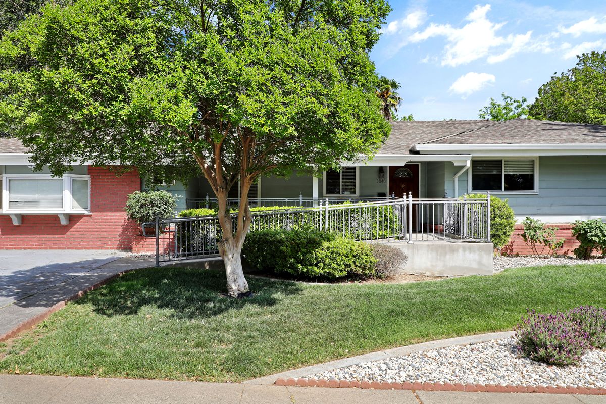 A suburban house with a front yard and a large tree, surrounded by a fence.