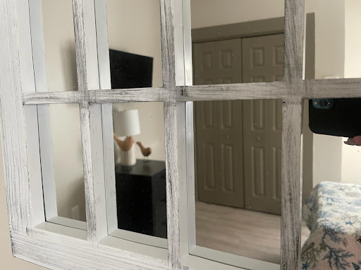 A view through a rustic window frame into a modern interior space featuring a lamp and furniture.