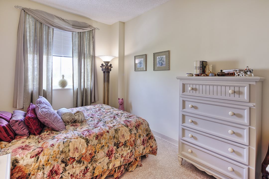 A cozy bedroom with floral bedding, a tall lamp, and a white dresser.