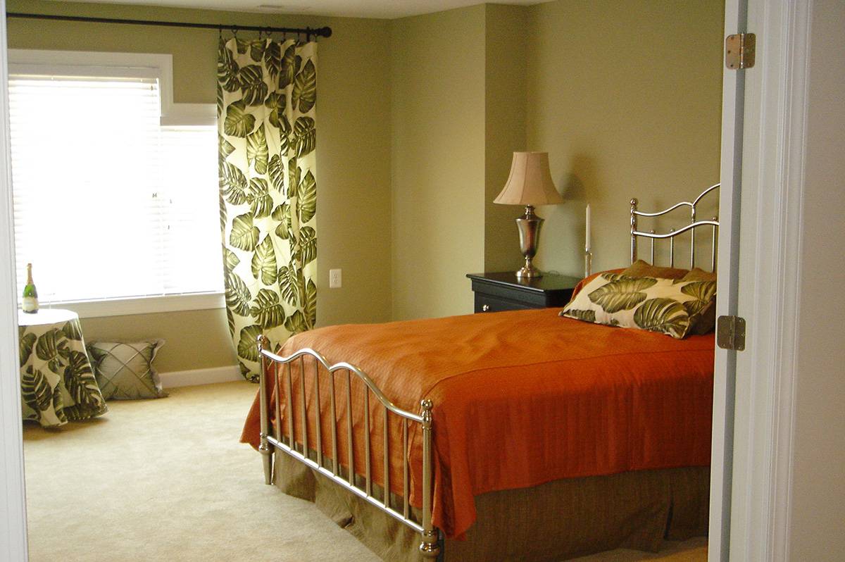 A cozy bedroom with an orange bedspread, leafy curtains, and a bedside lamp.