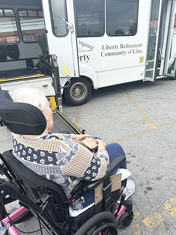 An elderly individual in a wheelchair awaits transportation from a community service.