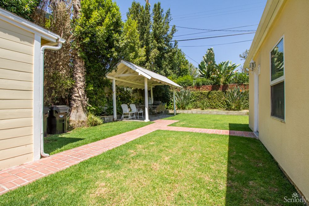 A well-maintained backyard with a lush lawn, shaded patio area, and vibrant trees.
