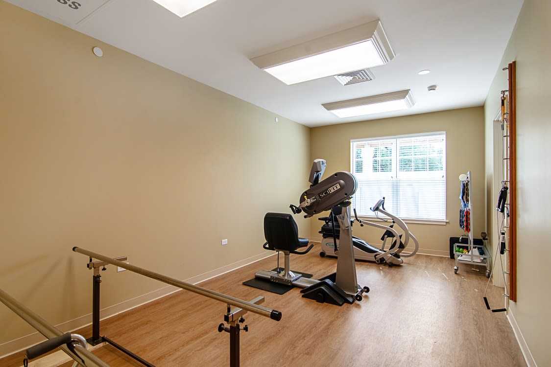 A well-lit rehabilitation room featuring exercise equipment, including a stationary bike and parallel bars.