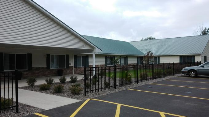 A building with a green roof and black fence, situated next to a parking lot under a cloudy sky.