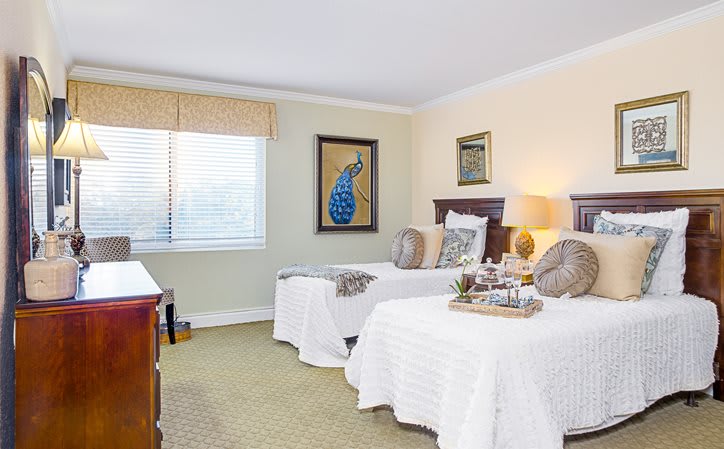 A cozy bedroom with twin beds, featuring elegant decor and a framed peacock artwork.
