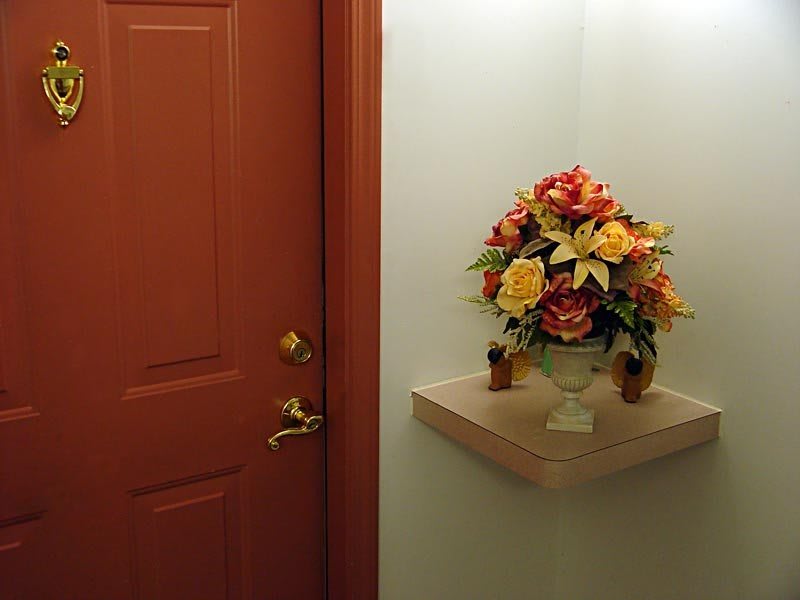 A corner of a room with a closed door and a floral arrangement on a shelf.