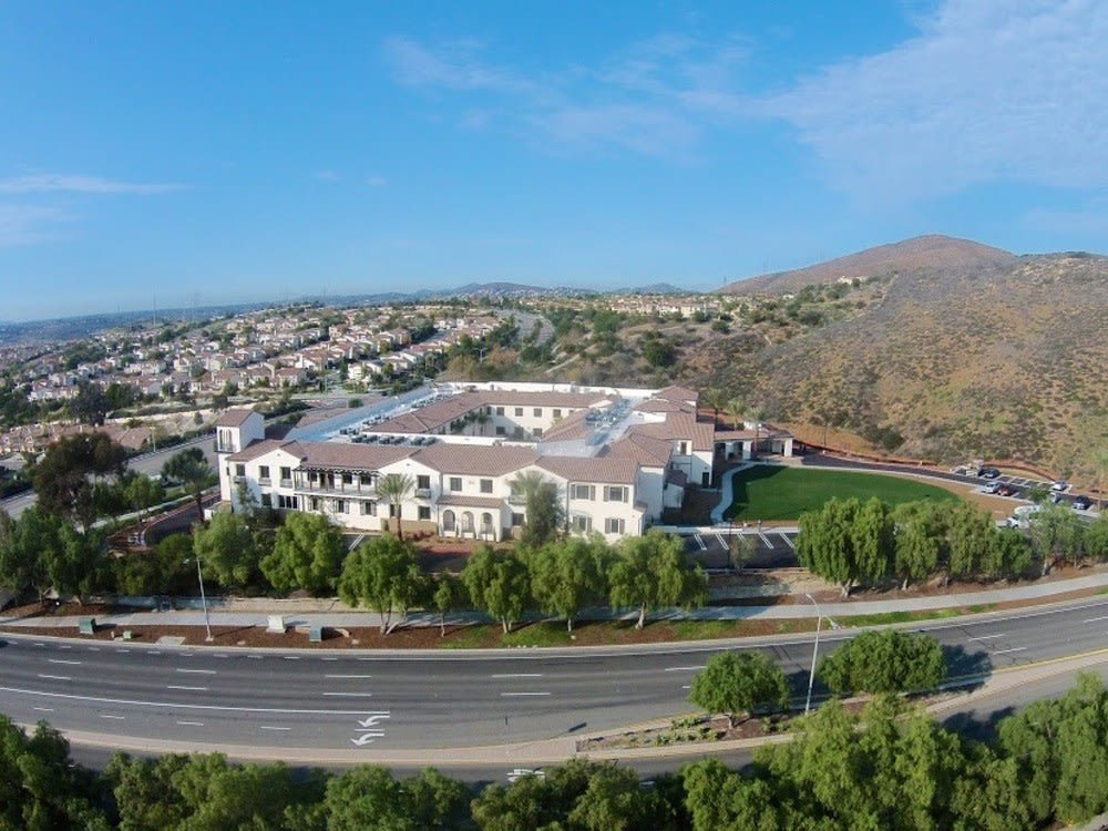 Aerial view of a large building surrounded by roads and residential areas with hills in the background.