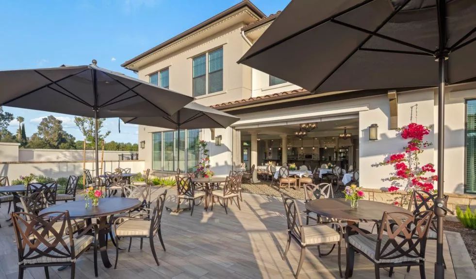 An inviting outdoor patio with tables, chairs, and large umbrellas, set against a modern building exterior.