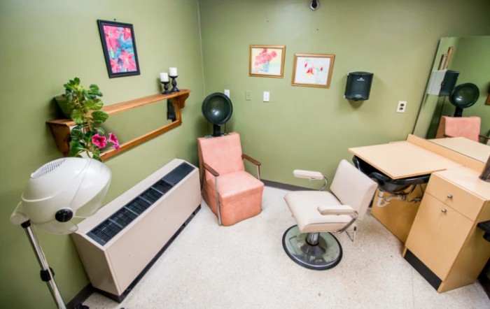 A cozy salon room with a hair dryer, chairs, and wall decorations.