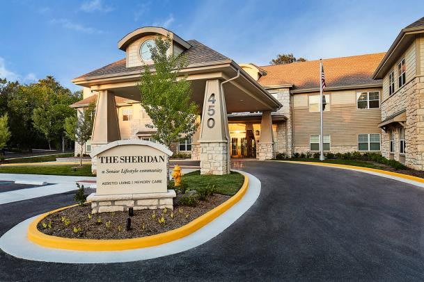 The entrance of a building with a visible sign and landscaped surroundings.