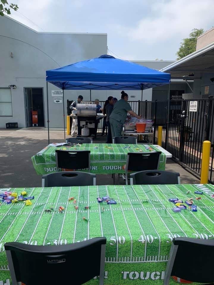 An outdoor party setup with a barbecue station under a blue tent and tables covered with themed tablecloths.