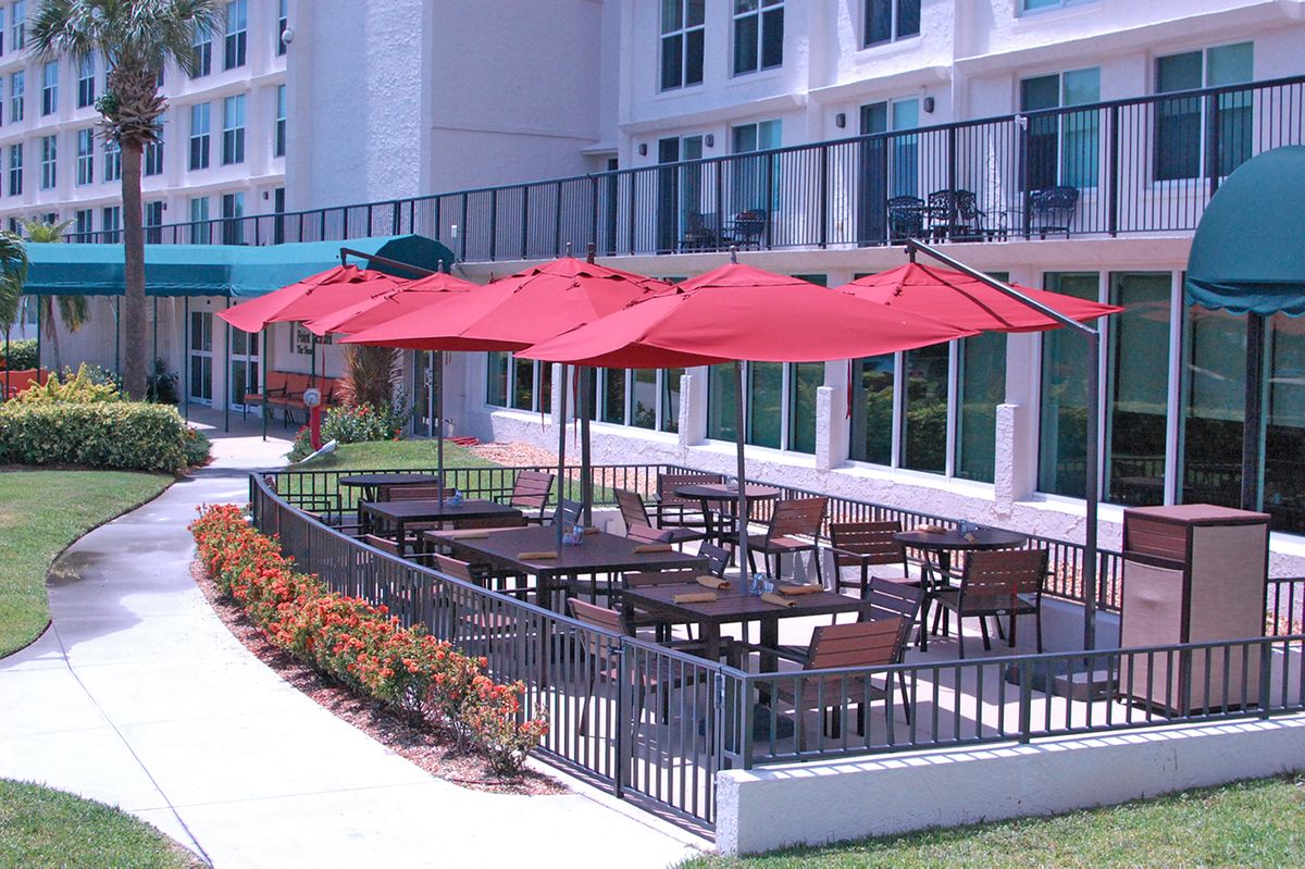 An outdoor restaurant patio with red umbrellas and neatly arranged tables and chairs on a sunny day.