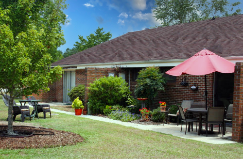 A cozy brick house with a landscaped garden and outdoor patio furniture under a large umbrella.