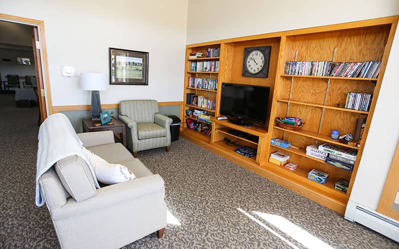 A cozy living room with comfortable seating and a wooden bookshelf featuring a TV, books, and decor items.