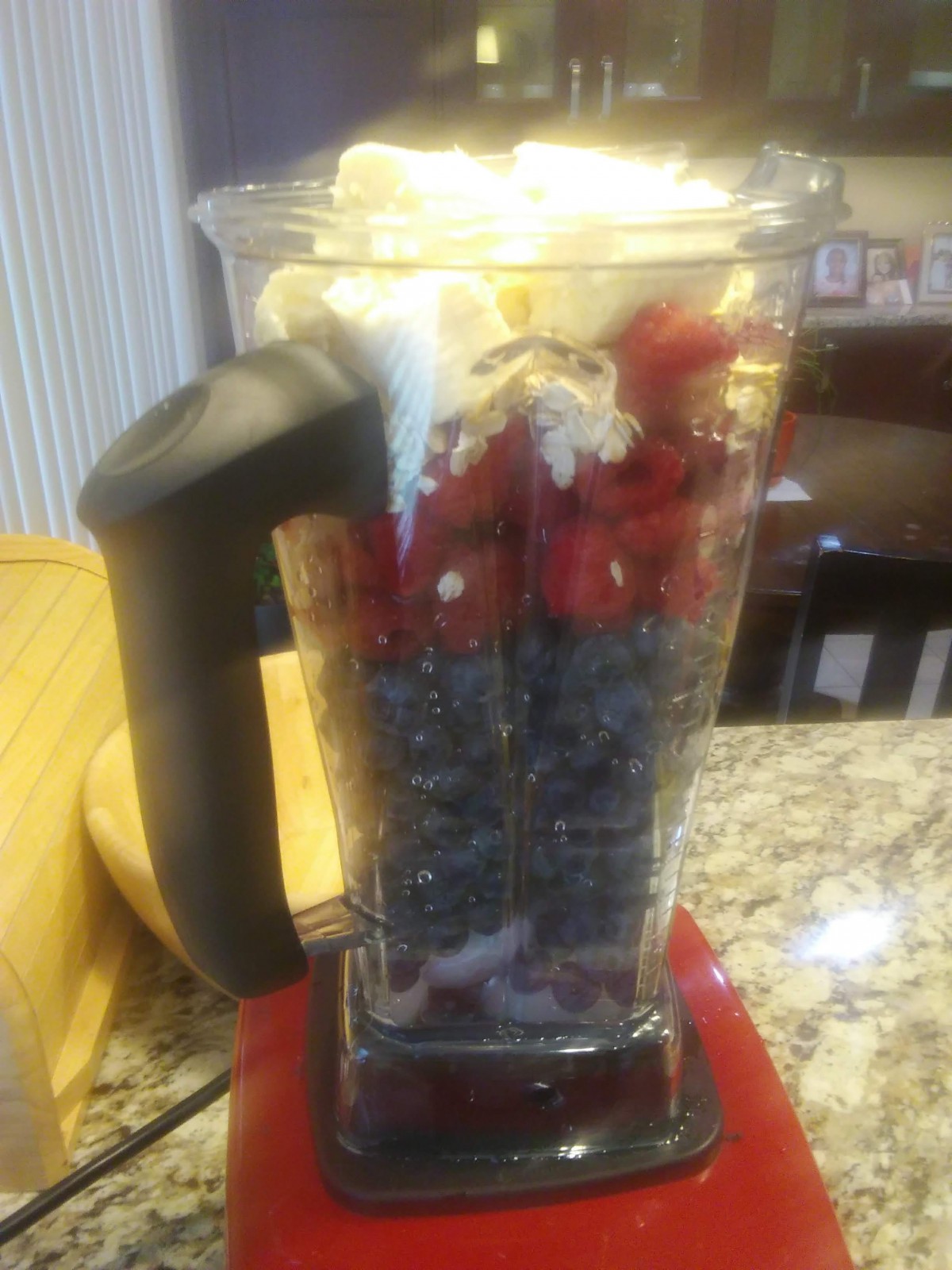 A blender filled with layers of blueberries, strawberries, and other smoothie ingredients in a kitchen setting.