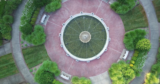 Aerial view of a circular fountain surrounded by lush greenery and benches in a park.