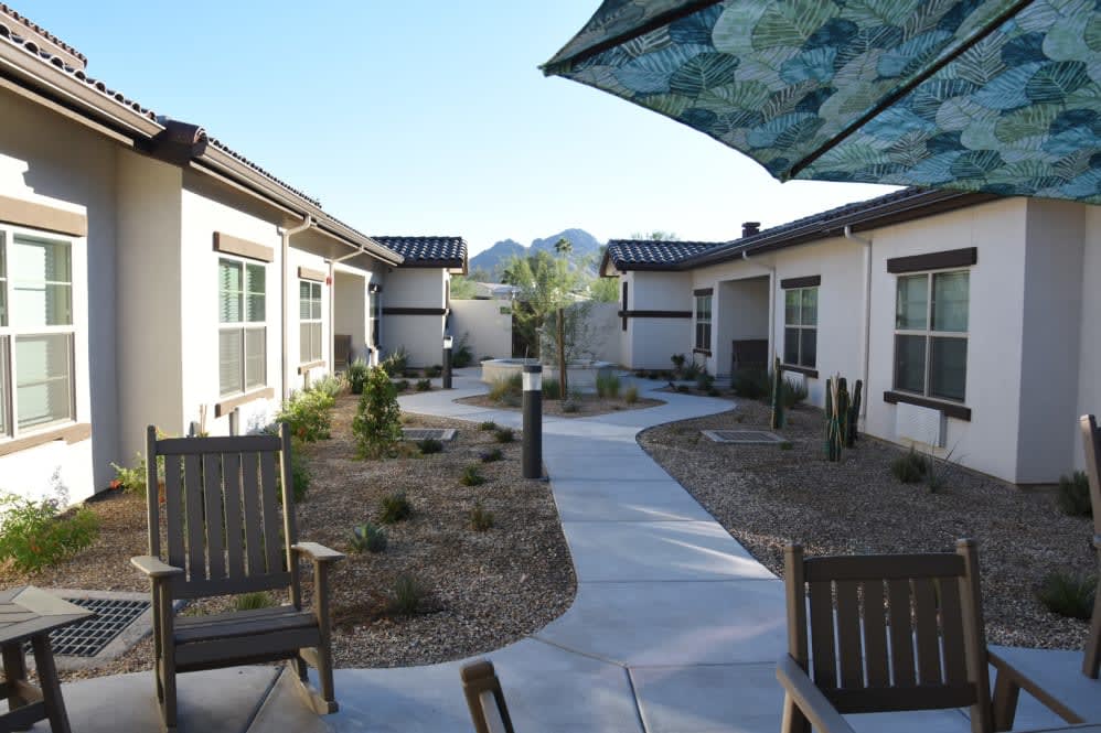 A serene courtyard with outdoor seating, surrounded by modern residential buildings and featuring a desert landscape with a mountain view.