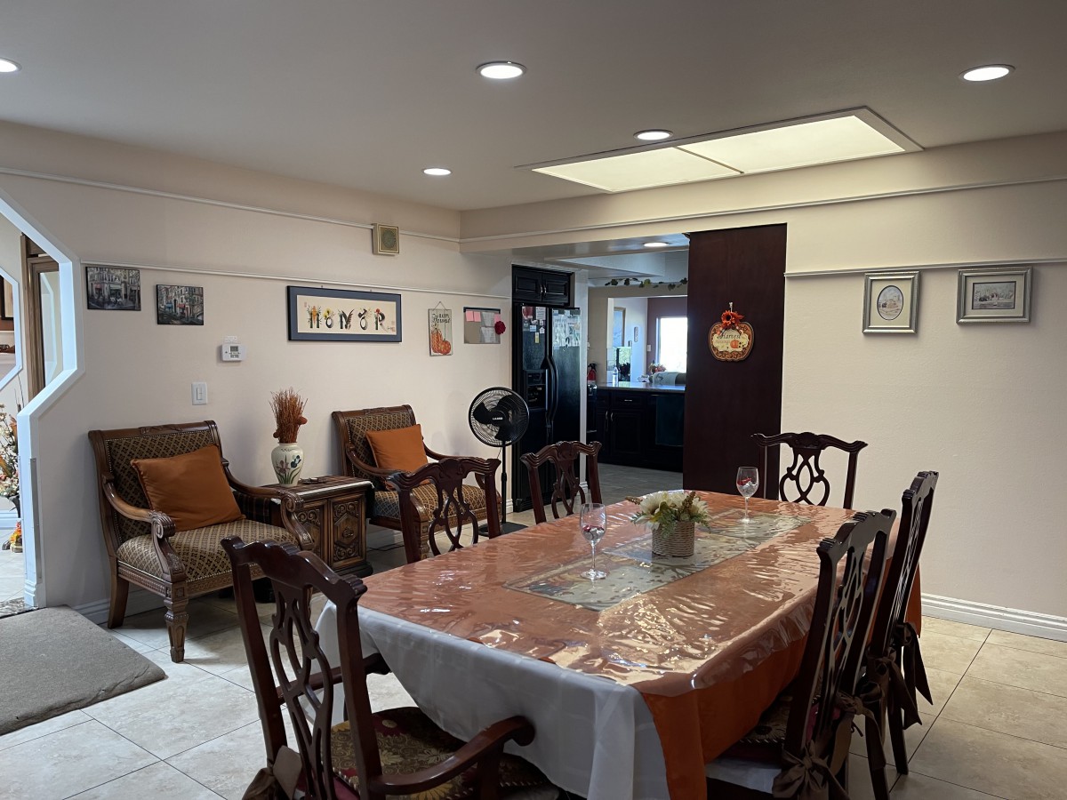 A cozy dining area with a large table, chairs, and comfortable seating, adorned with artwork and warm lighting.