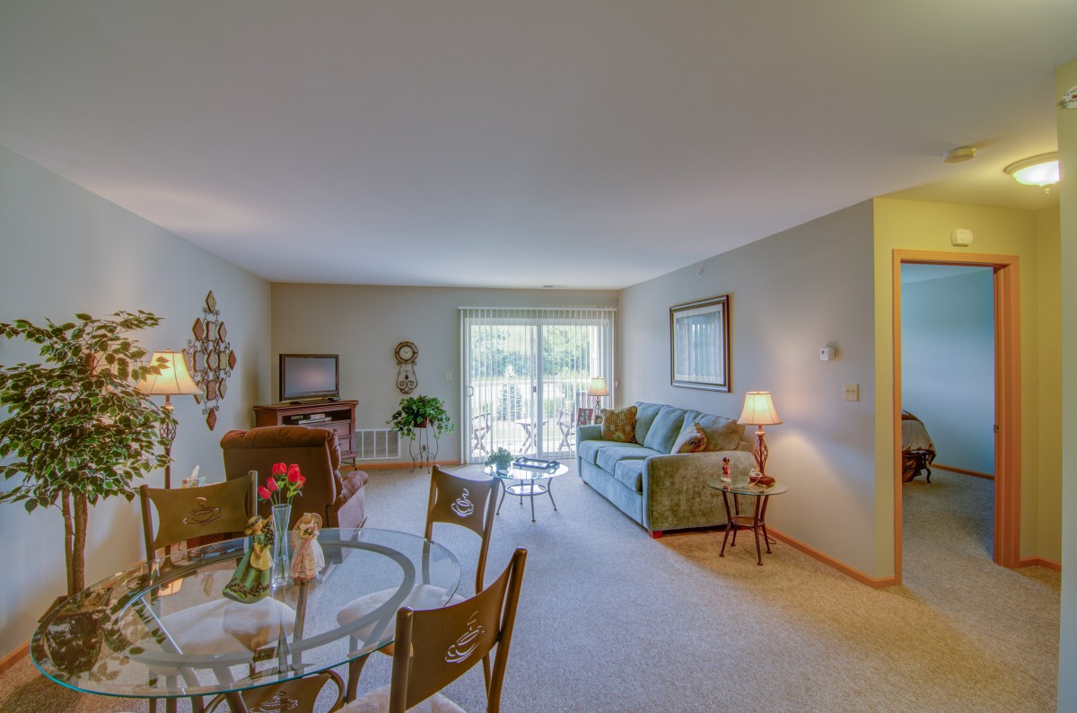 A cozy living room with a dining area featuring a sofa, glass table, and chairs, adorned with soft lighting and decorative elements.