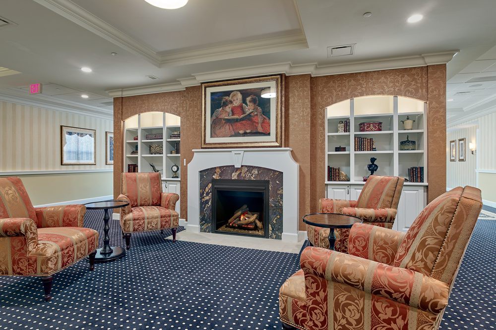 A cozy living room with a fireplace, surrounded by comfortable seating and decorated with elegant artwork and bookshelves.
