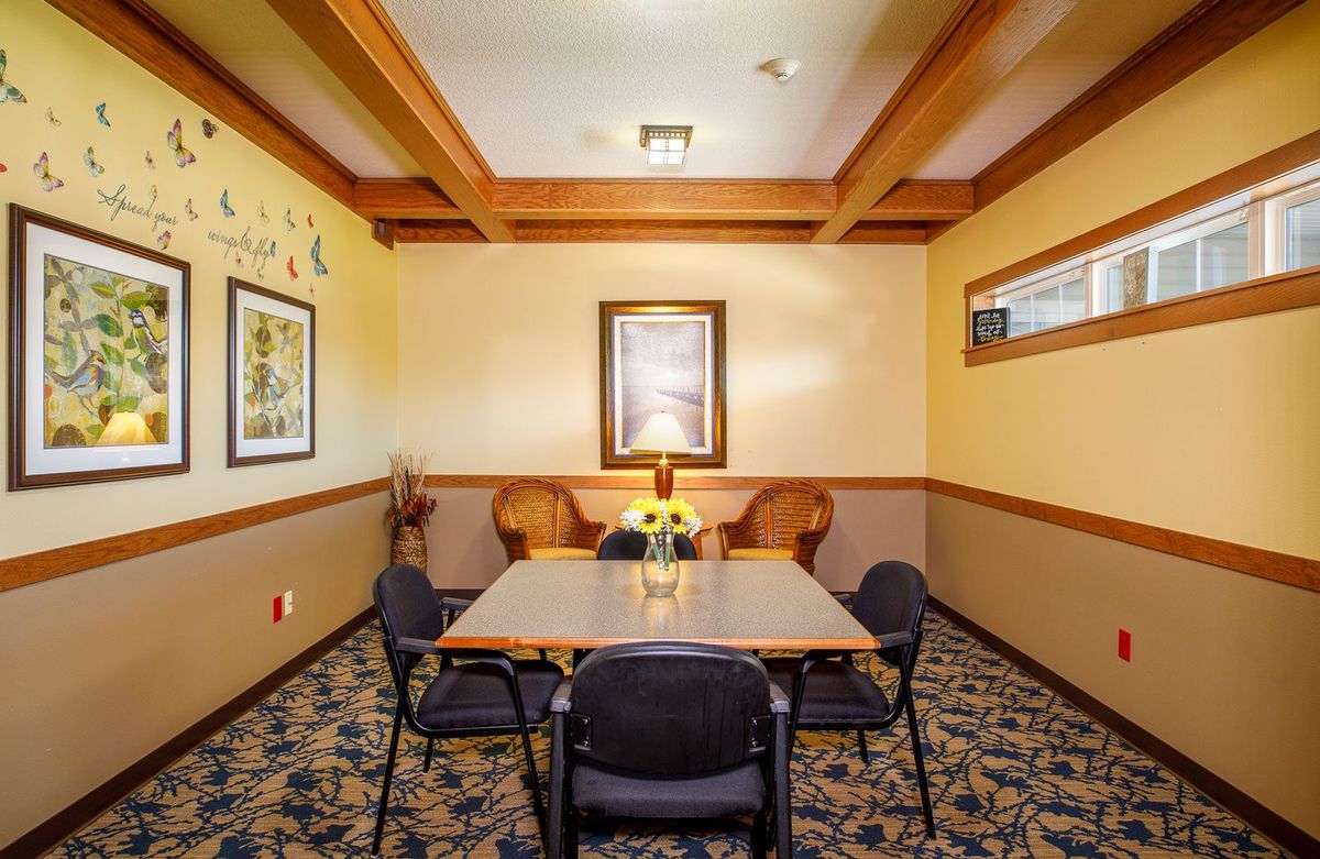 A cozy meeting room with a square table surrounded by chairs, featuring warm lighting and decorative elements.