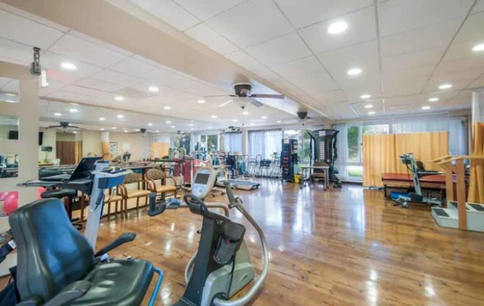 A spacious gym with various exercise equipment and a wooden floor.