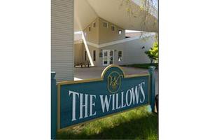 Entrance sign for The Willows with modern building in the background.