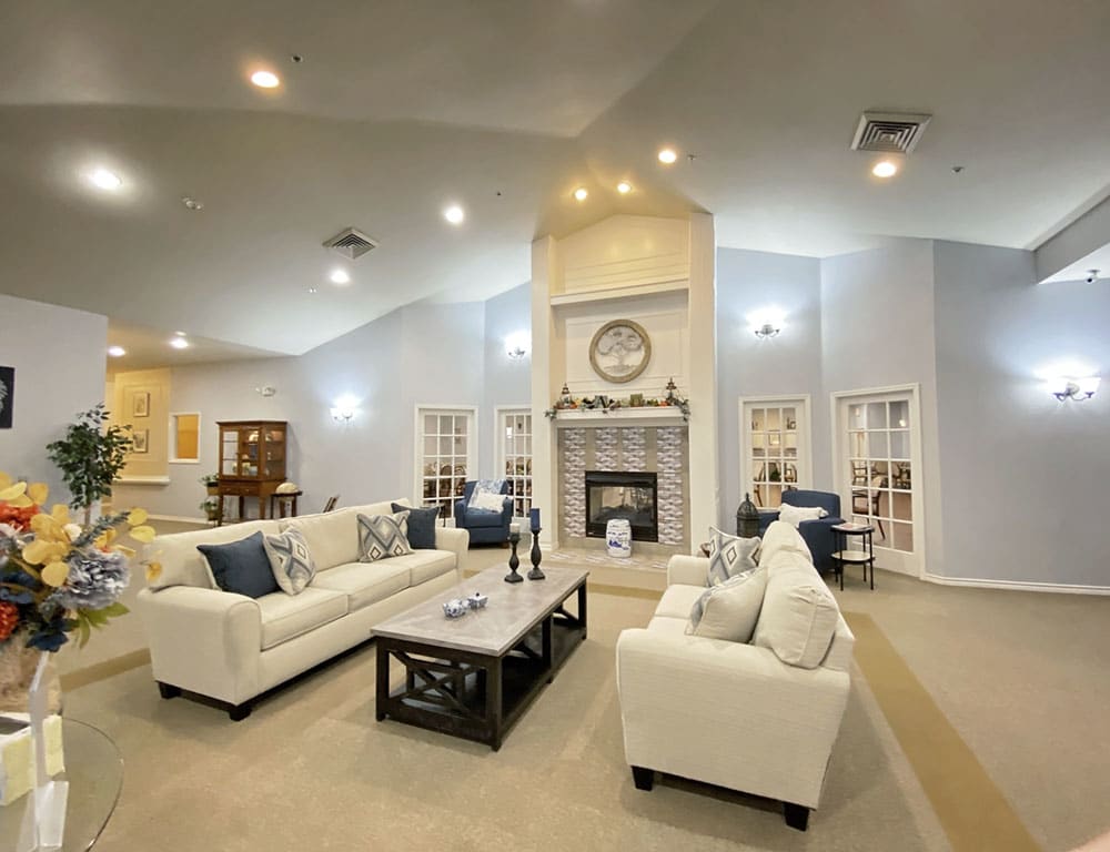 A modern living room with white couches, a central fireplace, and bright lighting.