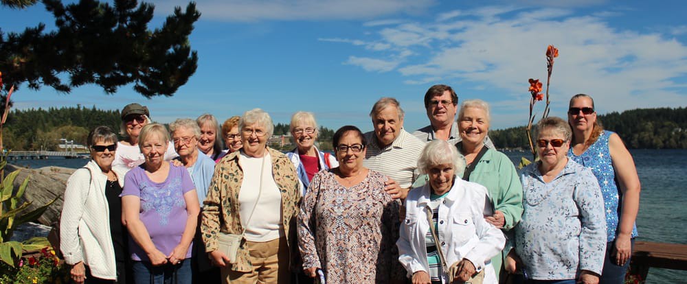 A group of seniors smiling together outdoors under a clear blue sky.