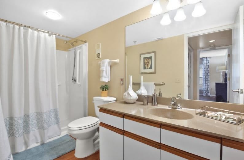 A modern bathroom with a large mirror, sink, shower, and decorative vases.