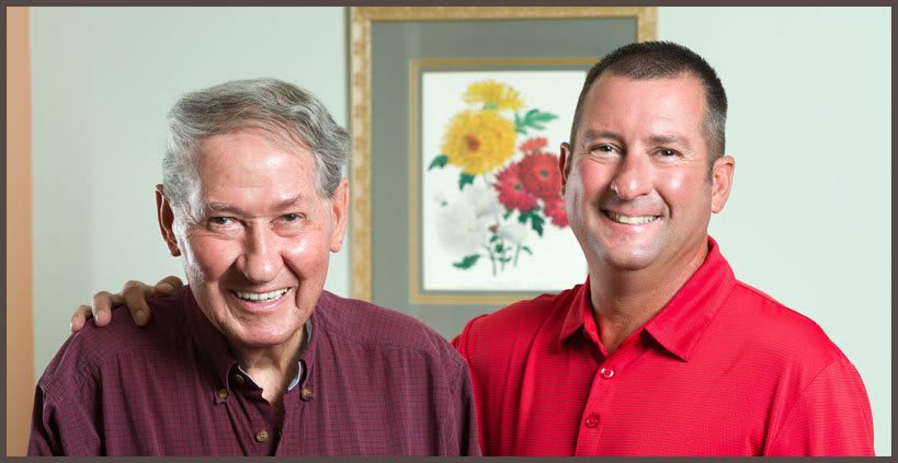 Two smiling people posing indoors with artwork in the background.