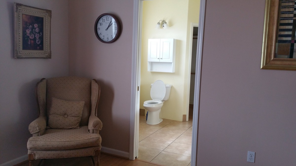 A view from a living room into a bathroom, with an armchair and a wall clock visible.