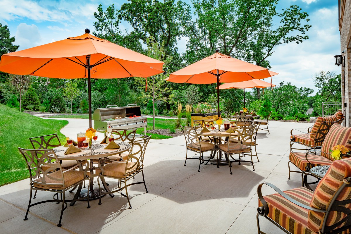 An inviting outdoor patio setup with tables and chairs under bright orange umbrellas surrounded by greenery.