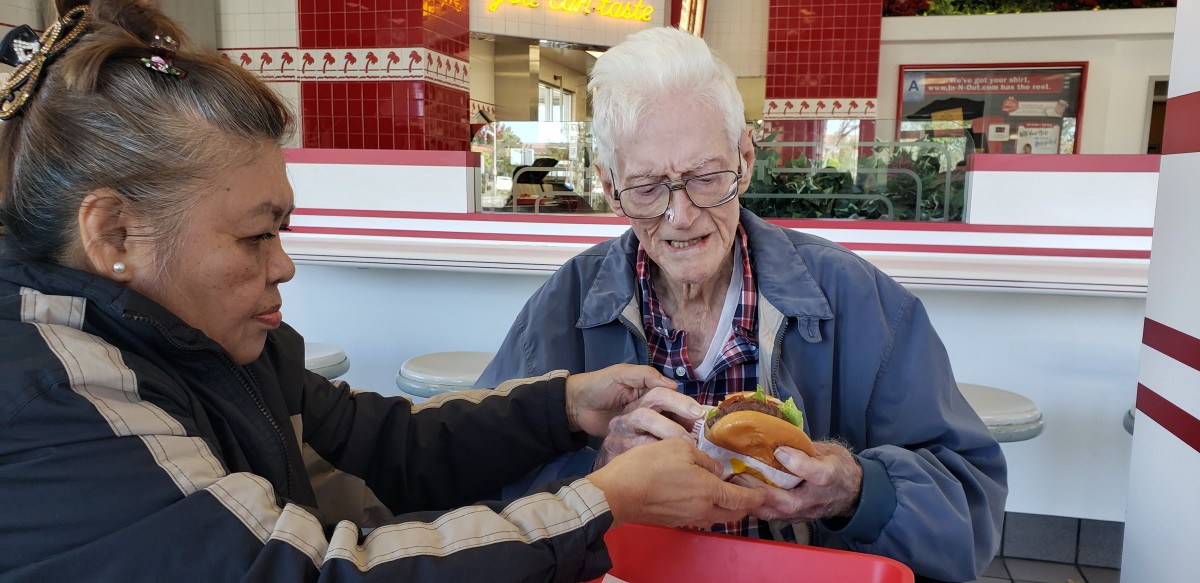 An elderly person is being handed a hamburger at a restaurant.