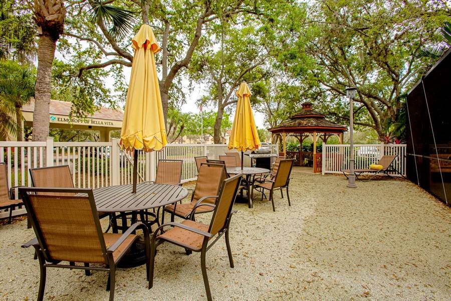 An outdoor patio area with tables and chairs shaded by yellow umbrellas, surrounded by lush trees.