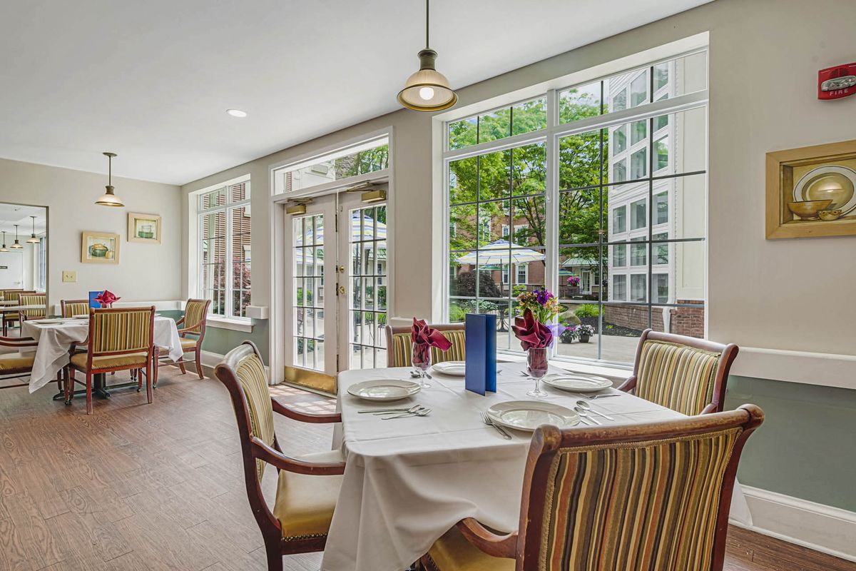 A well-lit dining area with a table set for four, overlooking a garden through large windows.