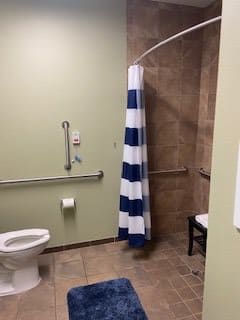 An accessible bathroom with a toilet, grab bar, and shower area separated by a striped curtain.