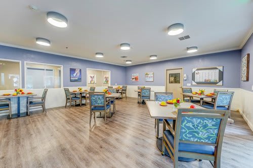A spacious and well-lit dining area with neatly arranged tables and chairs, featuring decorative wall art.