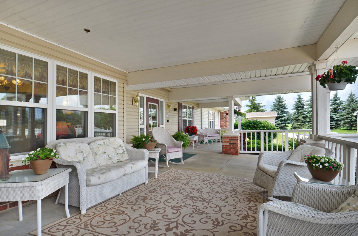 A cozy, covered porch with cushioned seating and potted plants.