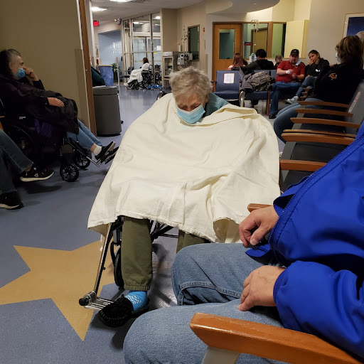 A patient sitting in a hospital waiting room, wrapped in a blanket while wearing a mask.