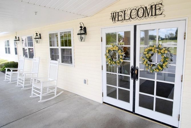 A warm and inviting porch with a welcome sign, adorned with wreaths on French doors and a white rocking chair.