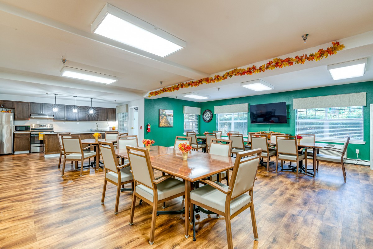 A spacious dining room with multiple tables and chairs, decorated with seasonal accents and equipped with a wall-mounted television.